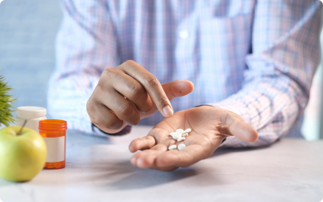 Hombre sentado con las manos sobre una mesa sosteniendo pastillas
